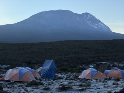 A row of mountaineering tents in front of Mount Kilimanjaro at dusk