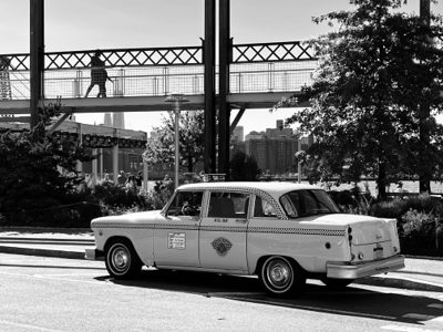 A vintage checkered taxi cab parked near a pedestrian bridge in New York City